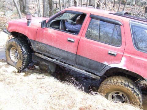 1976 Toyota Land Cruiser - This red SUV is navigating a difficult muddy terrain with its tires deep in the muck.