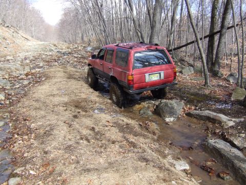 1976 Toyota Land Cruiser - A red SUV navigates a challenging off-road path with water and rocks.