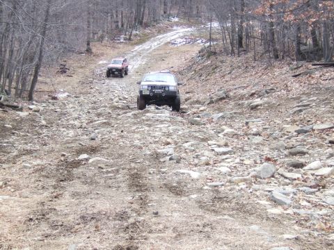 1976 Toyota Land Cruiser - Two SUVs tackle a challenging, rocky path through a wooded area.