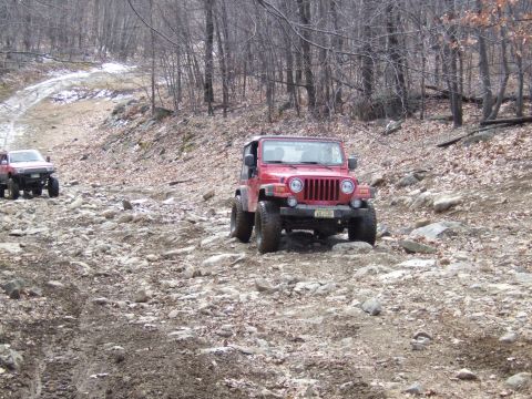 1976 Toyota Land Cruiser - Two off-road vehicles navigate a challenging, rocky terrain in a wooded area during daytime.