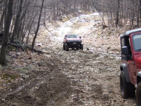 1976 Toyota Land Cruiser - Two off-road vehicles navigate a challenging rocky and muddy trail through a forest.