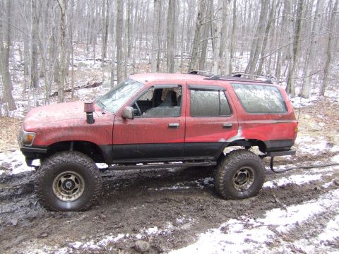 1976 Toyota Land Cruiser - Modified red SUV with snorkel and off-road tires navigating a muddy, wooded area.