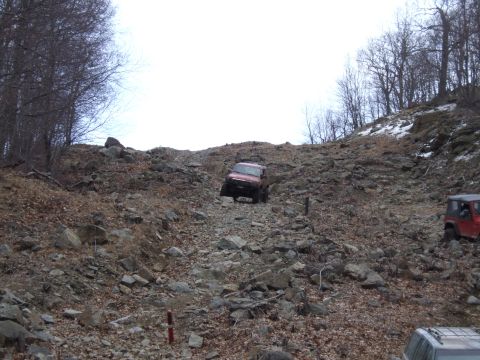 1976 Toyota Land Cruiser - Two off-road vehicles navigate a steep, rocky incline in a wooded area.