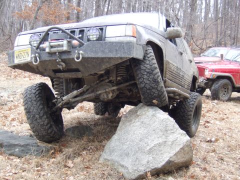 1976 Toyota Land Cruiser - Two modified Jeeps are shown off-roading, with one climbing over a large rock.