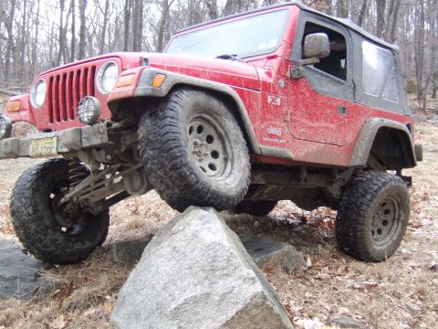 1976 Toyota Land Cruiser - A red Jeep Wrangler navigates a rocky trail, with one tire elevated on a large boulder.