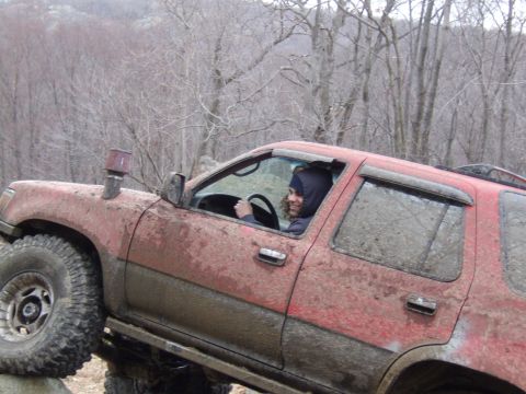 1976 Toyota Land Cruiser - A person drives a red SUV through a muddy off-road course.