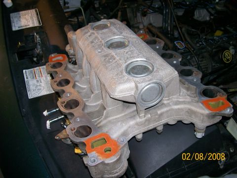 1995 Mercury Grand Marquis - A removed aluminum lower intake manifold resting on a fender cover, showing eight runner ports, machined sealing faces, capped plenum openi…