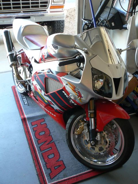1978 Ford Bronco - A red and silver Honda sport motorcycle is parked on a Honda branded mat inside a garage.