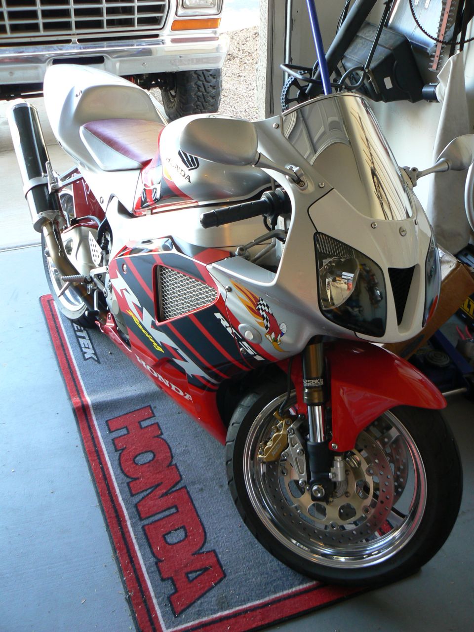 Red and silver Honda sportbike on a Honda mat. Truck in background