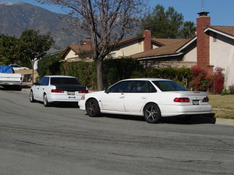 1992 Ford Taurus - Two white sedans are parked on a residential street, one with a black trunk lid.