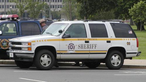 White Boone County Sheriff SUV parked next to a police SUV. Yellow stripe along the side