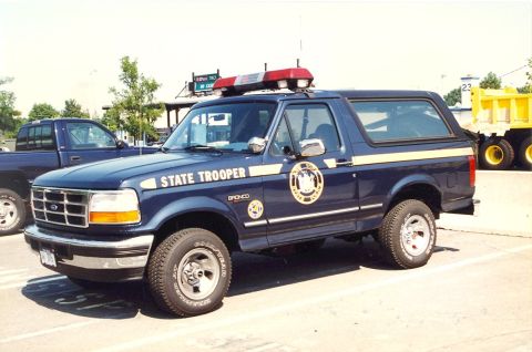 1991 Ford Crown Victoria - A Ford Bronco, marked as a State Trooper vehicle, is parked in a lot next to another truck.