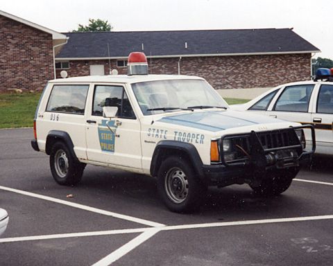 1991 Ford Crown Victoria - A white Jeep Cherokee marked as a State Trooper vehicle is parked next to another police car.