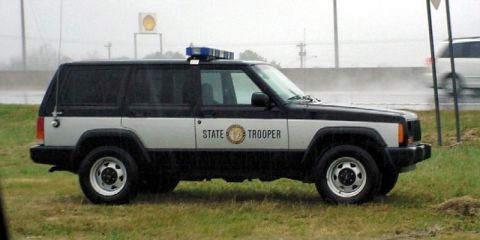 1991 Ford Crown Victoria - This Jeep Cherokee XJ is marked as a State Trooper vehicle and is parked on the side of the road.