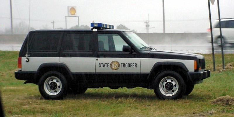 Side view of a black and silver Jeep Cherokee XJ with "STATE TROOPER" text and a light bar