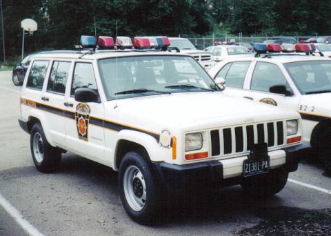 1991 Ford Crown Victoria - A white Jeep Cherokee police SUV is parked next to another police vehicle.