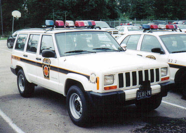 White Jeep Cherokee police SUV with light bar, side stripe, and Pennsylvania license plate 21381-PA