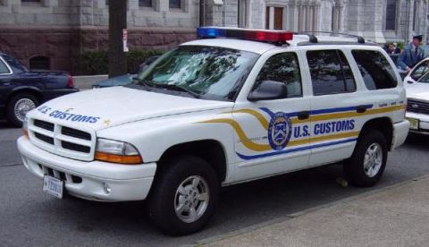 1991 Ford Crown Victoria - A U.S. Customs SUV is parked on a street, with other vehicles and a building in the background.