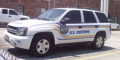 1991 Ford Crown Victoria - A white SUV with U.S. Customs livery is parked next to a white pickup truck.