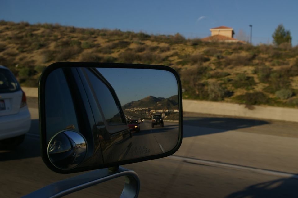 Black tow mirror with convex spot mirror reflecting freeway traffic and hills