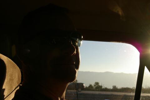 1986 Ford Bronco - A person gazes out of a car window at a hazy mountain landscape as the sun sets.