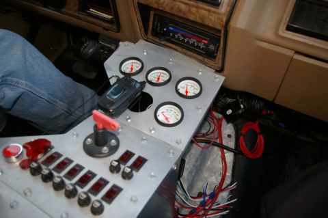 1986 Ford Bronco - A custom gauge cluster and array of switches are visible in the interior of a vehicle, alongside a cell phone.
