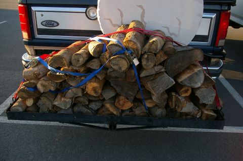 1986 Ford Bronco - A Ford pickup truck is shown from the rear, carrying a load of firewood secured with straps.
