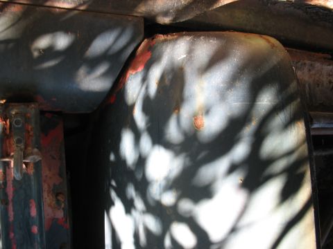 1949 Chevrolet C/K Pickup - Close-up of a weathered vehicle fender and a red-painted metal bracket, obscured by dappled light.