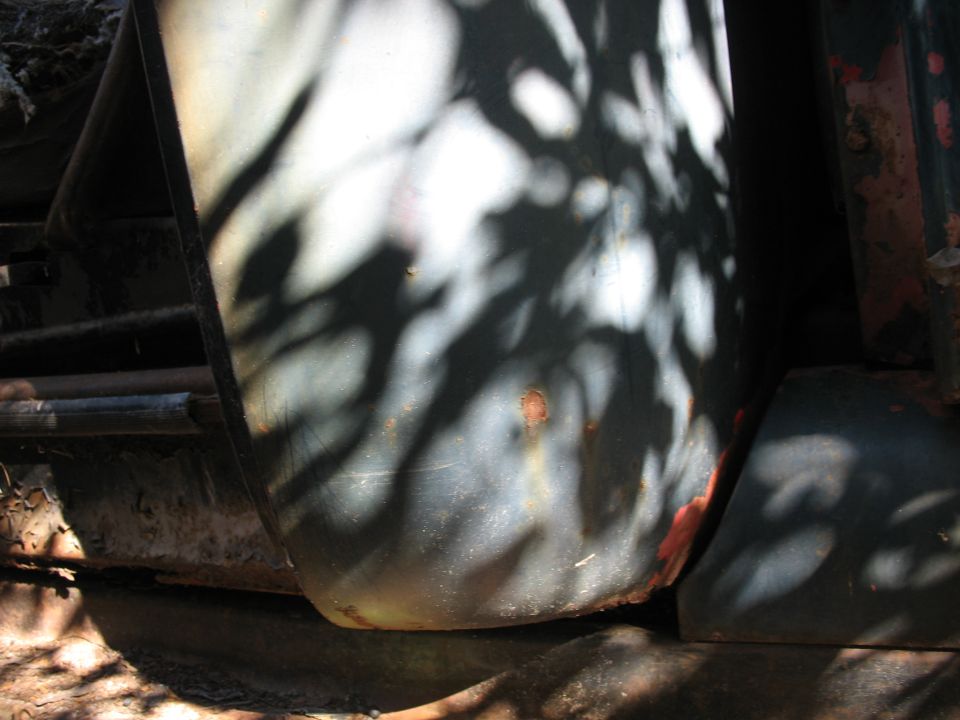 Close-up of a dark vehicle fender with rust spots and leaf shadows