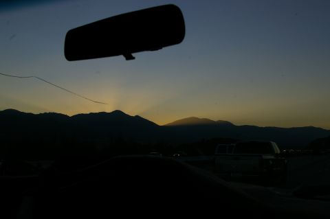 1986 Ford Bronco - View from inside a vehicle with a cracked windshield, looking out at a sunset over mountains. Another vehicle is visible in the distance.