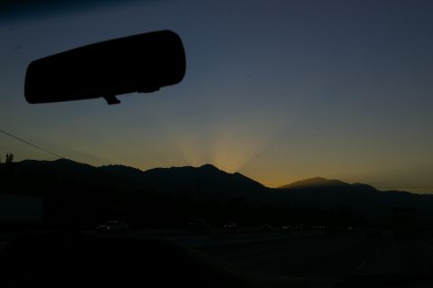 1986 Ford Bronco - Driving towards a mountain sunset, with the rearview mirror reflecting the fading light.