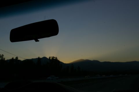 1986 Ford Bronco - The sun sets behind a mountain range, viewed from inside a vehicle.