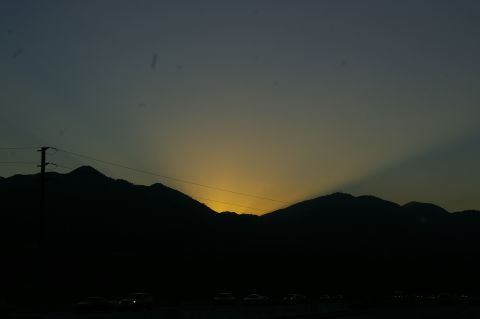 1986 Ford Bronco - A scenic view of a sunset behind silhouetted mountains, with a highway and traffic visible in the foreground.