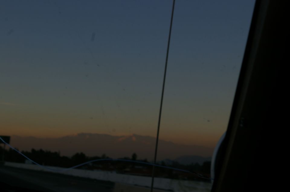 View from car interior at sunset with mountains and trees in distance