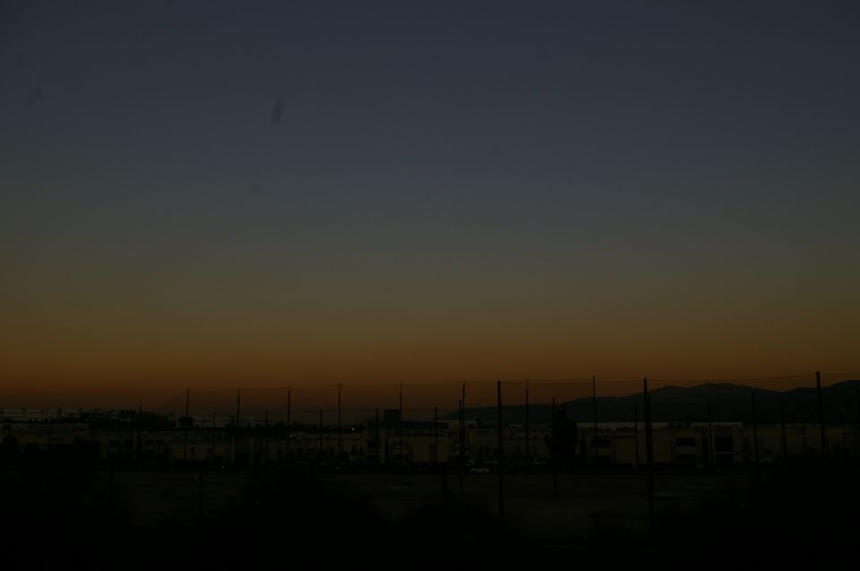 Sunset sky gradient over buildings and a fence line
