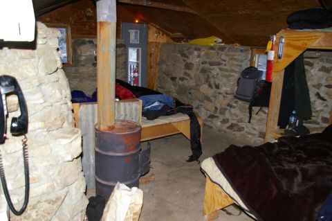 1986 Ford Bronco - The interior of a rustic cabin features sleeping bunks, a central wood-burning stove, and a wall-mounted telephone.