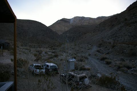 1986 Ford Bronco - Several vehicles sit abandoned in a desolate desert landscape under a pale sky.