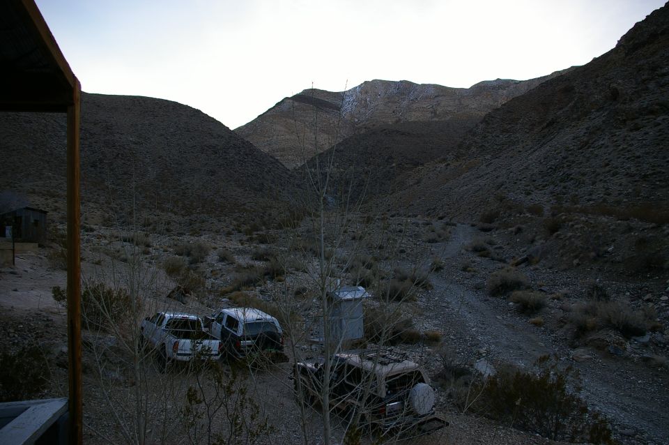 three old vehicles parked in a dry, rocky canyon with hills in the background