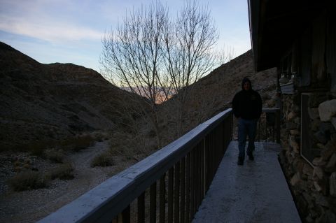 1986 Ford Bronco - A person walks along a walkway beside a stone building, with a desert landscape and bare trees visible in the twilight.