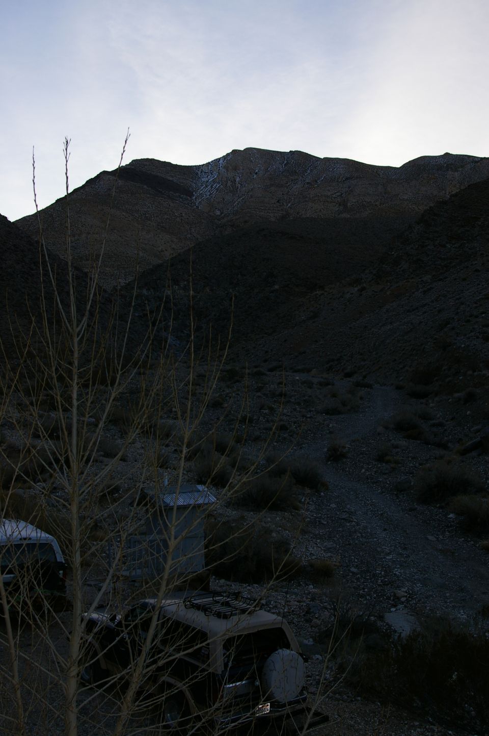 Two old vehicles sit abandoned in a dry, rocky desert landscape with mountains in the background