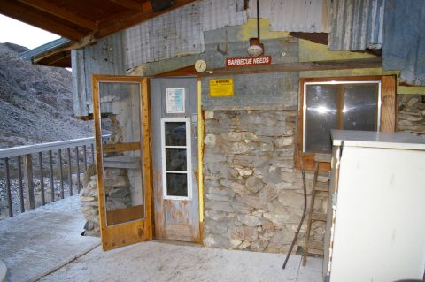 1986 Ford Bronco - Exterior view of a rustic cabin, possibly in a desert environment, with a sign indicating 'BARBECUE NEEDS'.