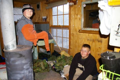 1986 Ford Bronco - Two young men in a rustic cabin with gear piled on the floor.