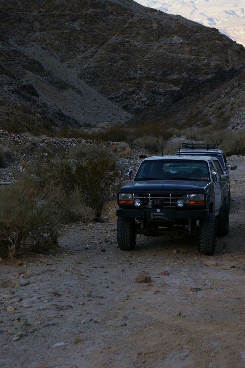 1986 Ford Bronco - Two Ford trucks are parked on a dirt road in a mountainous, arid landscape.