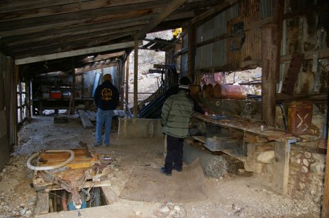 1986 Ford Bronco - Two individuals explore the interior of a decaying workshop filled with old equipment and debris.