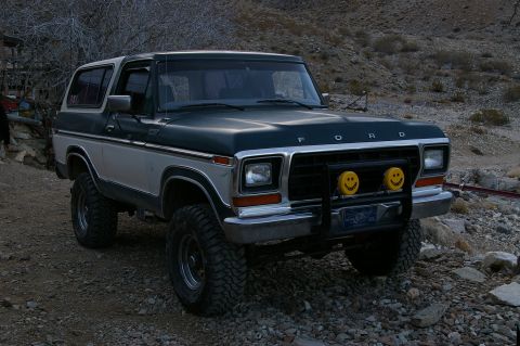 1986 Ford Bronco - This Ford Bronco is parked on a gravelly surface with sparse vegetation and rocky hills in the background.