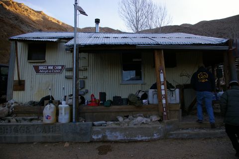 1986 Ford Bronco - Briggs Mine Cabin in a desert landscape, showing its rustic corrugated metal construction and surrounding environment.
