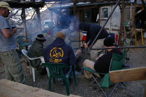 1986 Ford Bronco - A group of people are gathered around a fire pit, some sitting in chairs, near a corrugated metal structure.