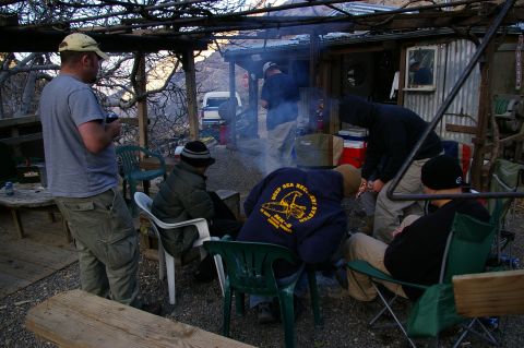1986 Ford Bronco - A group of people are gathered around a campfire at a rustic outdoor location, with a white pickup truck visible in the background.