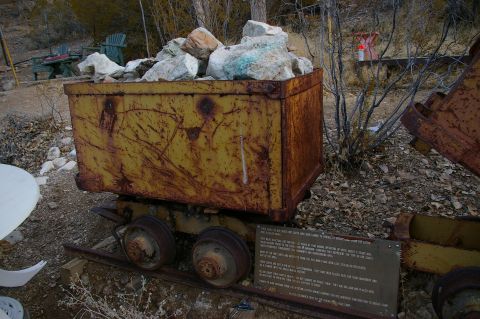 1986 Ford Bronco - A rusty mining cart sits on tracks, loaded with rocks, with a descriptive sign nearby.