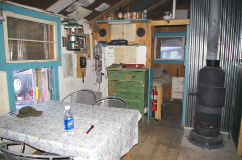 1986 Ford Bronco - The inside of a cabin shows a table set for a meal, a wood-burning stove, and a bed in the background.